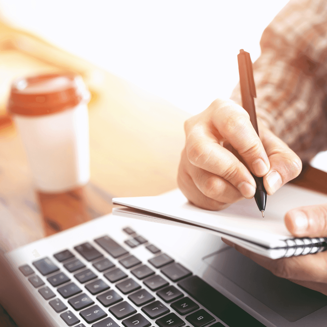 Writing on paper while using a laptop for online learning.